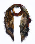 Presenting the “Da Vinci” scarf by SUZI ROHER—a lightweight, rectangular accessory with frayed edges. Digitally printed for sharp detail, this scarf showcases an abstract design in earthy browns, blacks, and subtle muted hues. Red text appears partially on the right side, adding unique flair to its artful look. Here, it is styled in a loose loop for a relaxed finish.