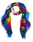 The SUZI ROHER "Sweet Love" scarf features a geometric patchwork in blue, yellow, red, green, and purple with scattered white letters and frayed edges, shown loosely looped on a white background.