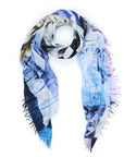 The Kim, Bella Giorno scarf by Suzi Roher is a lightweight, rectangular accessory with abstract blue, white, yellow, and purple patterns and frayed edges—ideal for adding carefree beach style to any outfit.