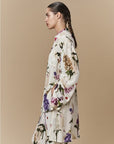 A woman with a long braid is shown in profile wearing HIGH’s Initiate botanical floral silk shirt and matching pants against a plain beige background.