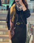 A women wearing a scarf with a black and white center and warm gold and Burgundy tones around the edge that falls down her black dress.