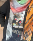Wearing SUZI ROHER’s Moda Florentina scarf, a black blazer, and a city-print shirt, this look captures chic Florence style. A decorative belt and dark jeans finish the outfit. The photo highlights details from shoulders to waist.