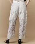 A person stands against a beige background, shown from the back wearing the HIGH Kick-Start wide leg lace pants with sheer embroidered panels, paired with a white top and black sandals.