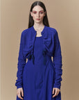A woman with long dark hair models the HIGH "Absolutely" dress, a royal blue fitted cardigan style with a textured finish, standing against a plain beige background and looking directly at the camera.
