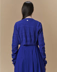 A person with long dark hair is shown from the back against a plain beige background, wearing the HIGH Absolutely blue seamless knit cardigan and matching dress.