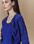 A woman with long brown hair wears bright red eyeshadow and the HIGH Absolutely royal blue fitted textured cardigan over a matching top, posed against a neutral beige background.