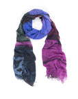 The SUZI ROHER "Color Is Everything" scarf, made of modal wool in abstract blue, purple, green, and black with frayed edges (200 x 70 cm), is displayed in a loose loop on a white background.