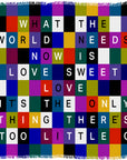 The “Sweet Love” scarf by SUZI ROHER features a vibrant grid design, each square displaying a letter from the iconic phrase: WHAT THE WORLD NEEDS NOW IS LOVE SWEET LOVE.