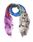 The Wild West scarf by SUZI ROHER is a lightweight modal silk accessory featuring an abstract design in blue, teal, orange, purple, and gray, finished with fringed edges for a modern take on cowboy style.