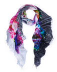 The SUZI ROHER Garden Party scarf is a lightweight, oversized Italian silk piece with fringed edges, featuring pink, purple, and blue florals on one side and black-and-white diagonal stripes on the reverse.