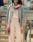 Woman wearing a light pink blouse and pants, and the "Love You Always" scarf by SUZI ROHER, showcasing an abstract floral pattern in black, gray, pink, red —a meaningful gift for any occasion. She is in an indoor setting.