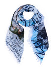 The SUZI ROHER "To Enjoy" scarf is lightweight with frayed edges, featuring abstract blue and black lines, handwritten-style text, and a painted section of classical figures—ideal for daily wear or as a gift.