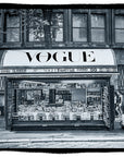 A SUZI ROHER “Lily, Vogue Italia B&W” artwork depicts a city street newsstand with a prominent VOGUE sign, selling magazines and newspapers. Nearby, scooters and a motorcycle are parked—all rendered in striking black and white.