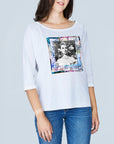 A woman wears The Bailey by SUZI ROHER—a 100% cotton, boxy tee with a colorful square graphic of a black-and-white vintage Audrey Hepburn—paired with blue jeans against a light gray background.