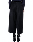 A person, seen from the back against a plain white background, wears High’s Sleek high-waisted wide-leg black cropped trousers with a dark long-sleeve top and black platform-heeled boots.