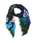 The SUZI ROHER “Spanish Vogue” scarf displays original artwork with a scenic print in blue, green, and white hues, featuring a visible road sign marked 88. Digitally printed for vibrant detail and finished with frayed edges, this colorful accessory is shown on a white background.