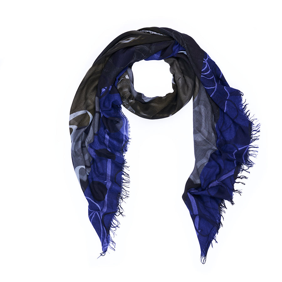 The SUZI ROHER Style Icon scarf features a dark blue and black palette with subtle patterns and frayed edges, arranged in a loop on a white background; its understated style perfectly channels the classic tomboy look made famous by Katharine Hepburn.