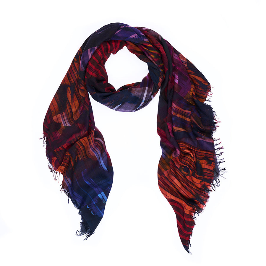 The “True to Form” scarf by SUZI ROHER features a vibrant striped pattern in red, orange, blue, and purple hues, digitally printed from original artwork. Loosely draped in a loop with frayed edges, it is showcased against a white background.