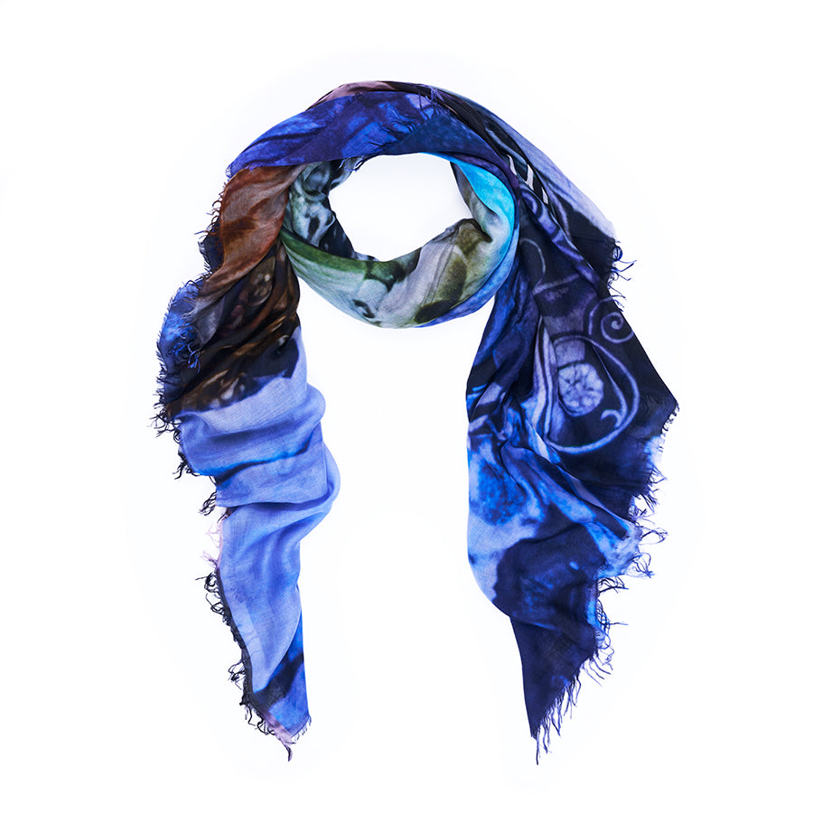A square scarf from SUZI ROHER, named “Sunset Blvd.,” features frayed edges and showcases a vibrant blue and multicolored abstract pattern inspired by original artwork. Digitally printed, the scarf is draped in a loose loop against a white background.