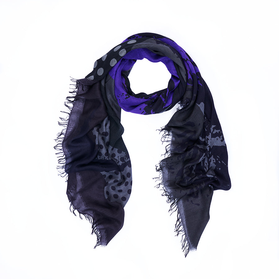 Here’s the rewritten sentence using your product data: The “Lucy” scarf by SUZI ROHER is displayed in a loose circular shape on a white background, showcasing its black and purple hues with fringed edges, adorned with polka dot and abstract patterns inspired by original digitally printed art.