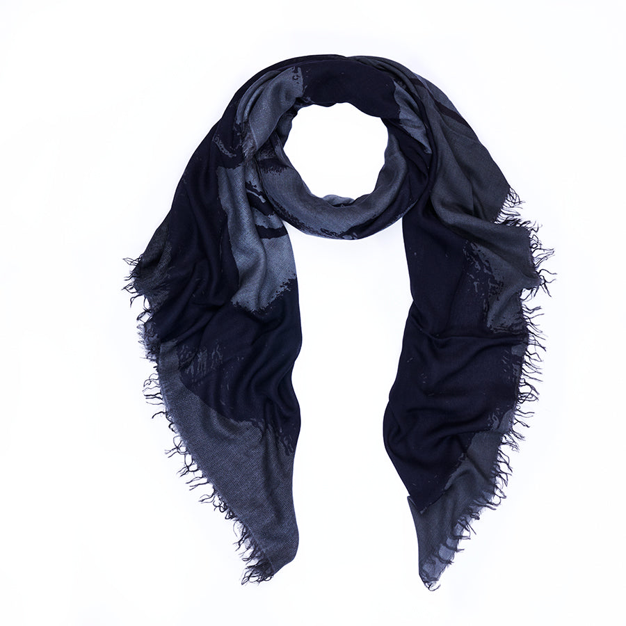 A SUZI ROHER Elizabeth B&amp;W scarf, featuring digitally printed original artwork in dark blue and black with frayed edges, is arranged in a loose loop on a white background.