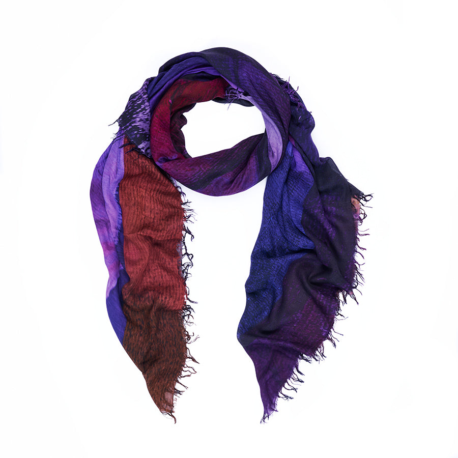 Introducing the AH! scarf by SUZI ROHER—a lightweight accessory with frayed edges, artfully arranged in a twisted loop against a white background. This statement piece features digitally printed original artwork and displays a striking gradient of deep purple, blue, and reddish-brown hues for a truly distinctive touch.