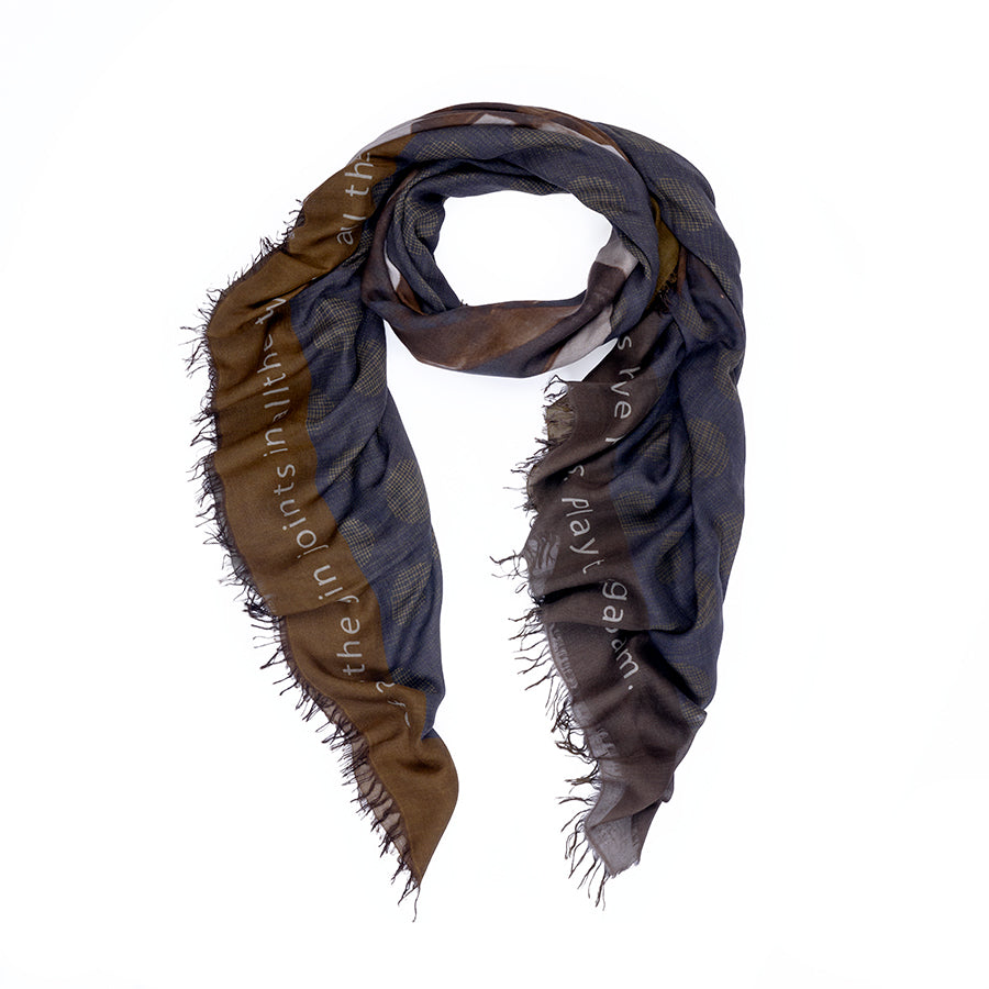 The Play It Again scarf by SUZI ROHER features brown and blue checkered patterns with frayed edges, draped in a U-shape on a white background. Digitally printed original artwork and partially visible faded white text accent the design.