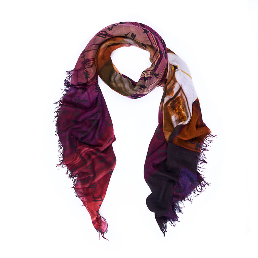 The SUZI ROHER “Scarlett” scarf, lightweight and multicolored with frayed edges, is loosely arranged in a loop against a white background. Featuring abstract patterns in shades of purple, red, orange, and black accented by handwritten text, its vibrant design is inspired by original artwork and digitally printed for exceptional detail.