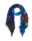 The “Opera” scarf by SUZI ROHER is a colorful rectangular accessory with frayed edges, featuring abstract patterns and partially visible text in a range of hues. Digitally printed from original artwork, it is shown arranged in a loose loop on a white background.
