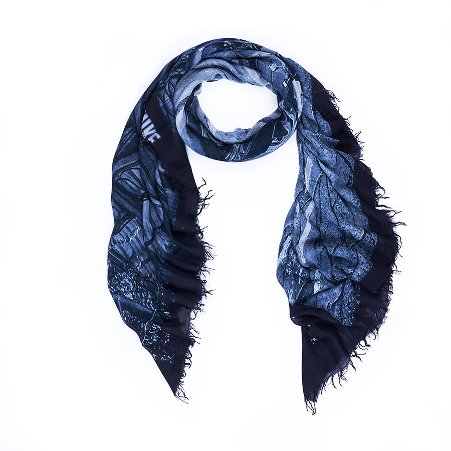 The SUZI ROHER Vogue Italia B&amp;W is a dark blue and black fringed scarf featuring a textured, abstract pattern inspired by Milan artwork, elegantly arranged in a loose oval shape on a white background.