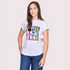 A smiling woman with long brown hair wears SUZI ROHER's The Karlie—a white T-shirt with a colorful THE ARTIST graphic—paired with blue jeans, standing against a light, plain background.