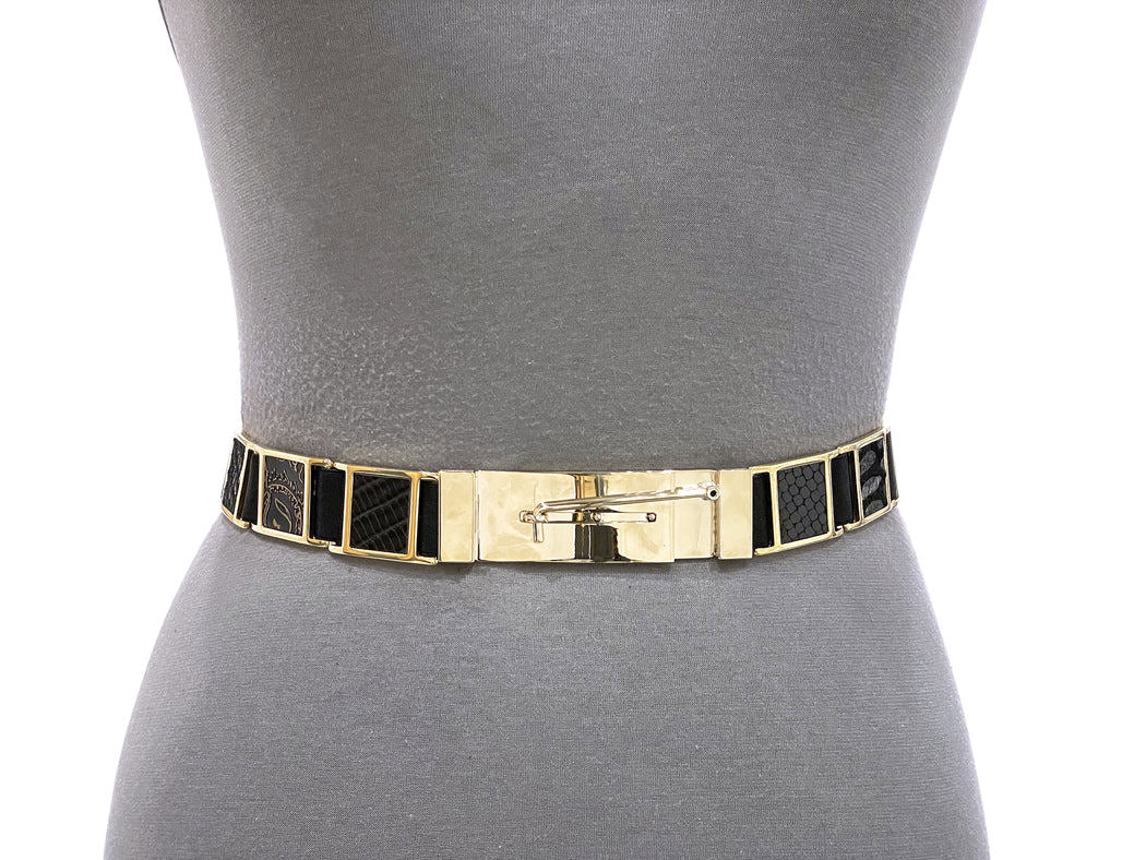 The SUZI ROHER "Brandy" belt is a chic gold and black leather accessory with geometric patterns, bold gold hardware, and a safety pin buckle, shown here on a gray dress form torso.