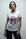 A woman with light brown hair in a loose updo wears The VIV Tee By You by SUZI ROHER, a customizable V-neck with a colorful modern lounge graphic, standing against a plain light background and facing the camera neutrally.