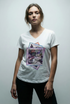 A woman with light brown hair in a loose updo wears The VIV Tee By You by SUZI ROHER, a customizable V-neck with a colorful modern lounge graphic, standing against a plain light background and facing the camera neutrally.
