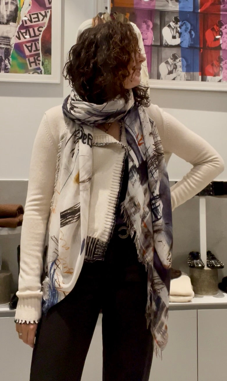 Women wearing The Elizabeth St. scarf by SUZI ROHER is a lightweight Italian accessory with frayed edges, showcasing an abstract black, white, beige, blue, and orange pattern and styled in a soft loop.