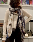 Women wearing The Elizabeth St. scarf by SUZI ROHER is a lightweight Italian accessory with frayed edges, showcasing an abstract black, white, beige, blue, and orange pattern and styled in a soft loop.