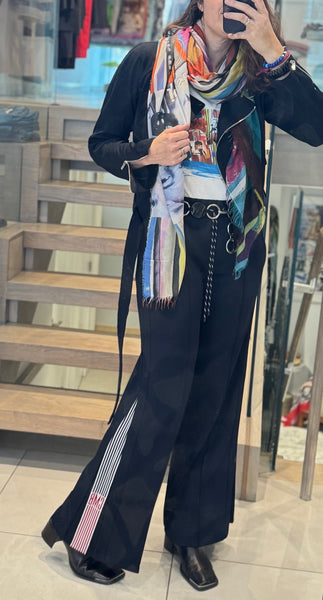 Person wearing a colorful scarf and black outfit with wide-leg pants in an indoor setting.
