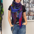 Channeling American singer Borns, a person wears SUZI ROHER's Lila, Electric Love scarf—a colorful accent with a black tee featuring a multicolored design and blue jeans with chain detail. Black-and-white photos appear in the background.