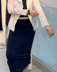 Indoors, a person adjusts the sleeve of their HIGH Affair Jacket with lace sleeves, styled with a navy maxi skirt, black top, white belt, and white sneakers.