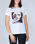 A woman models The Niki by SUZI ROHER: a classic 100% cotton white tee with Audrey Hepburn’s black-and-white face graphic and a red heart on her cheek, paired with black pants against a plain background.