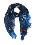The Rest Between Notes scarf by SUZI ROHER is a luxury modal silk piece made in Italy, featuring a blue pattern with frayed edges and accents of red and white text, shown loosely coiled on a white background.