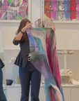 Women putting on a Multi-colored scarf with a tie-dye feather pattern by SUZI ROHER, 145 square. 