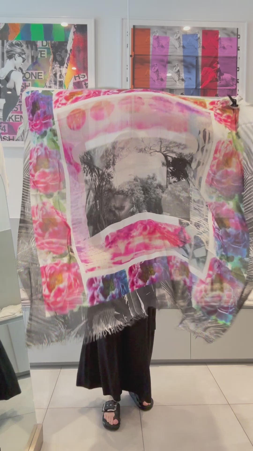 A women showing a beautiful scarf with a black and white center, surrounded by bright pink flowers. Then wrapping the scarf on her outfit. 