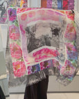 A women showing a beautiful scarf with a black and white center, surrounded by bright pink flowers. Then wrapping the scarf on her outfit. 