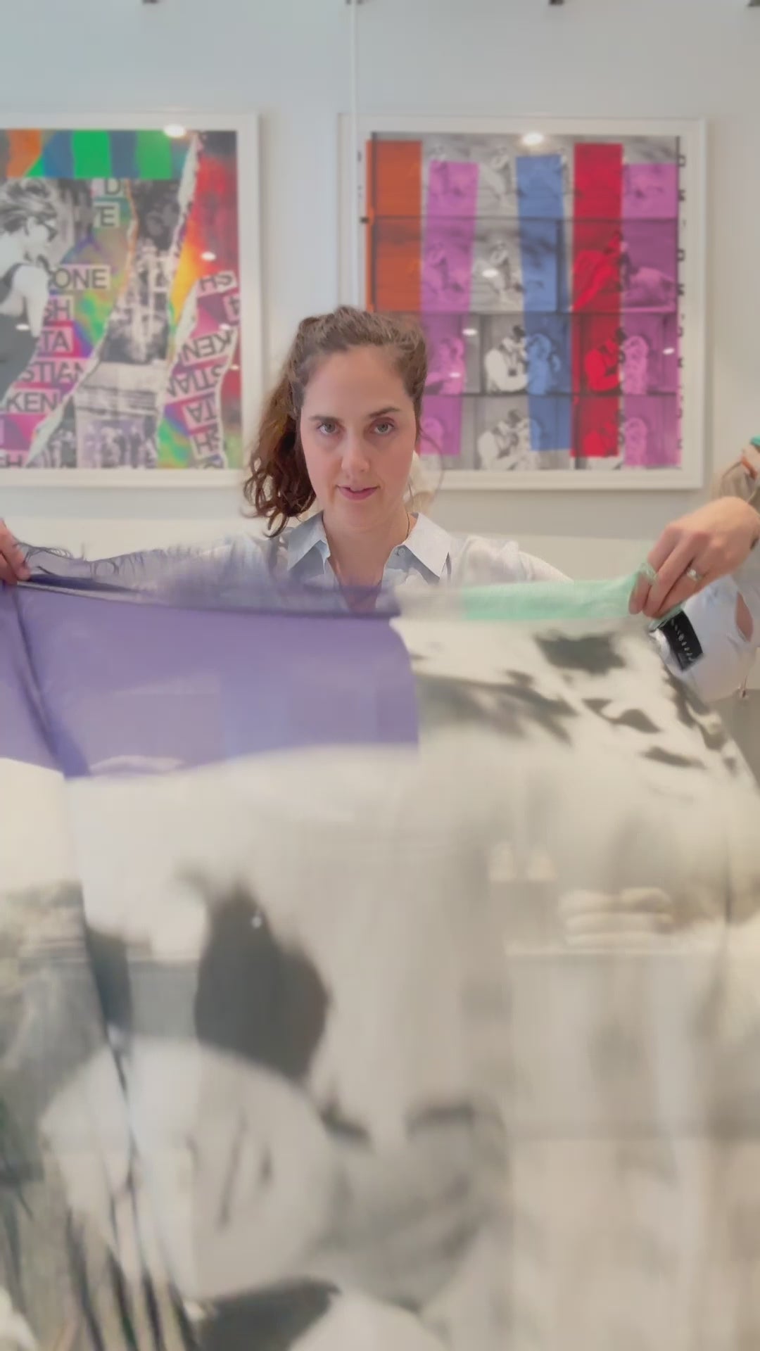 A video of a women tying a small blue-grey scarf on. She is tying the scarf into a tie. 