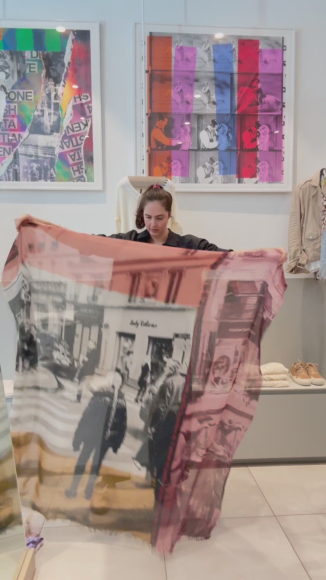 A women showing the Color of Love scarf, featuring  multicoloured abstract pattern—burgundy, gold, pink, black, and cream with frayed edges and a soft texture. She then wraps it around her neck.
