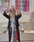 A video of a women putting on a the SUZI ROHER just a second scarf. The SUZI ROHER Just a Sec scarf features frayed edges and a vibrant, multicolored abstract design, recalling old Hollywood glamour with its swirling stripes—a timeless style inspired by icons like Audrey Hepburn and Marilyn Monroe.