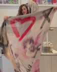 A women wrapping the scarf The Love You Always scarf by SUZI ROHER. It features classical cherubs overlaid with graffiti text—O, X, red heart, "TI AMO," "i love you,".
