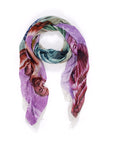 The Suzi Roher "Shar, Buddha - colors" silk scarf displays vibrant digital patterns in purple, green, red, and beige, artfully looped with draped ends against a white background.
