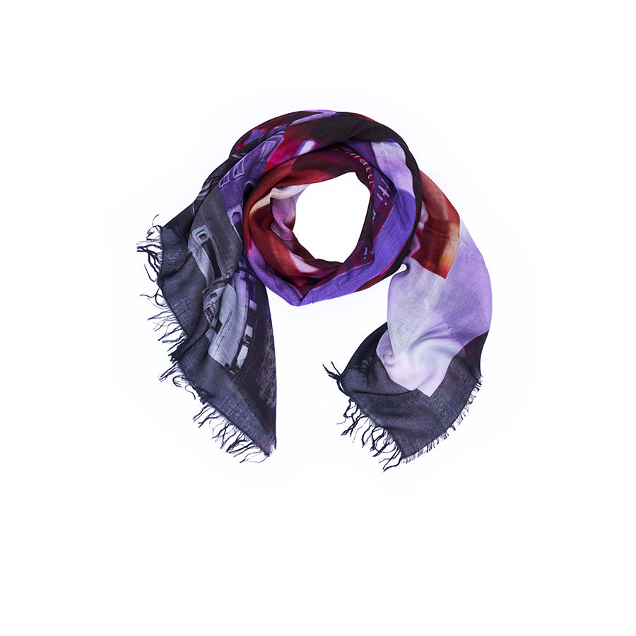 The SUZI ROHER “Lily, Tutti Matti” scarf—a square accessory with frayed edges—features a vibrant abstract design in purple, red, and black hues, reminiscent of original artwork found on an Italian postcard. It is displayed in a loose loop on a white background.